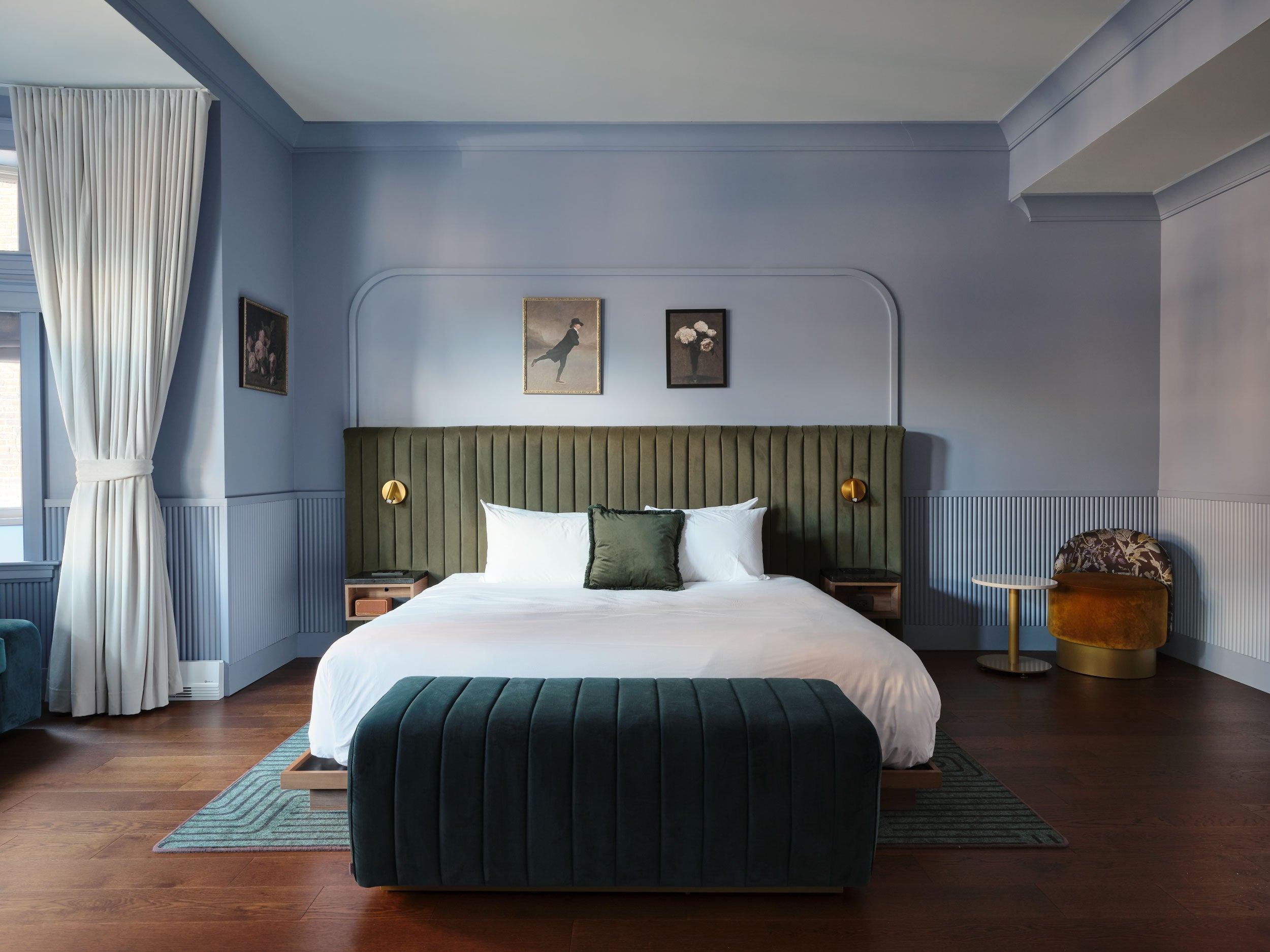 Chambre élégante et moderne d’un hôtel de luxe, avec un lit king-size, tête de lit vert olive, murs bleu pastel, parquet en bois foncé, fauteuil design et éclairage chaleureux, Hôtel Maurice.