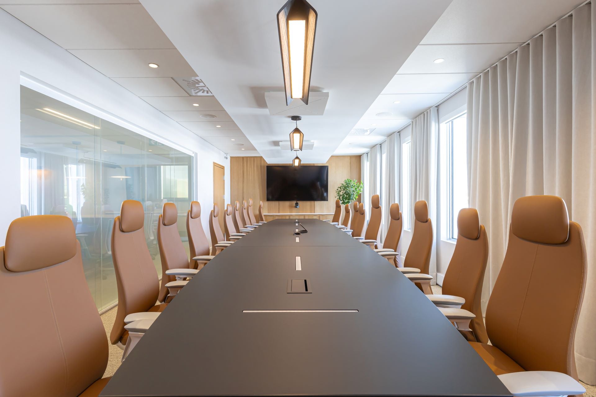 Salle de conférence moderne avec table ovale en noire et chaises ergonomiques en vinyle caramel - mobilier de réunion contemporain avec cloisons vitrées et éclairage LED suspendu