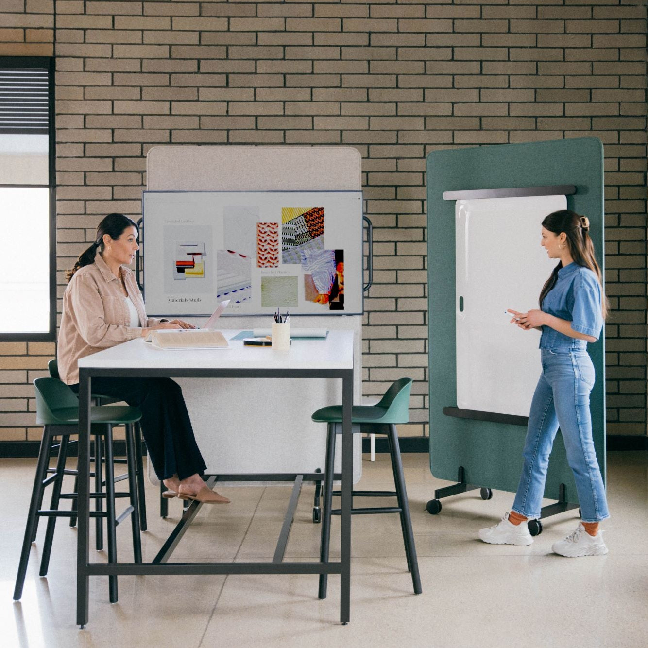 Salle de réunion collaborative avec table haute, tableau mobile et mobilier moderne. Deux collègues échangent autour d’un espace de travail créatif et flexible.