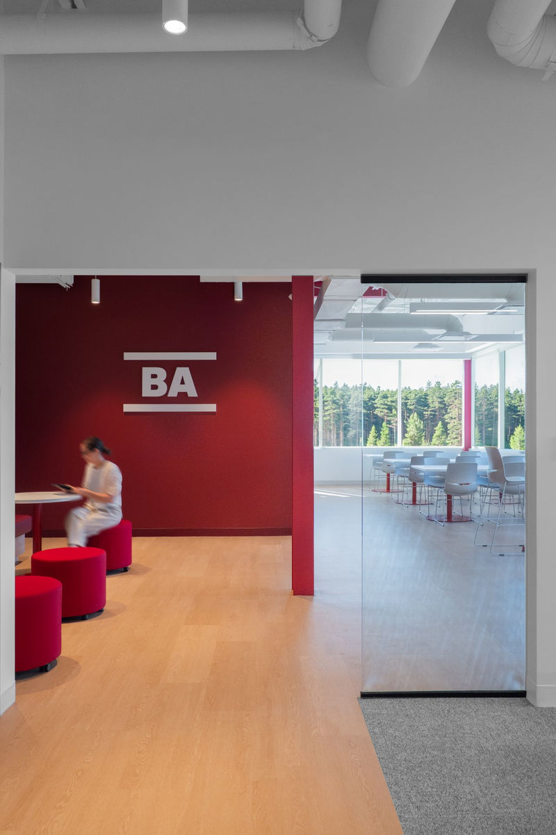 Espace de travail collaboratif avec mur d'accent bordeaux, logo BA, poufs rouges et salle de réunion vitrée avec vue sur la forêt — Beauce Atlas