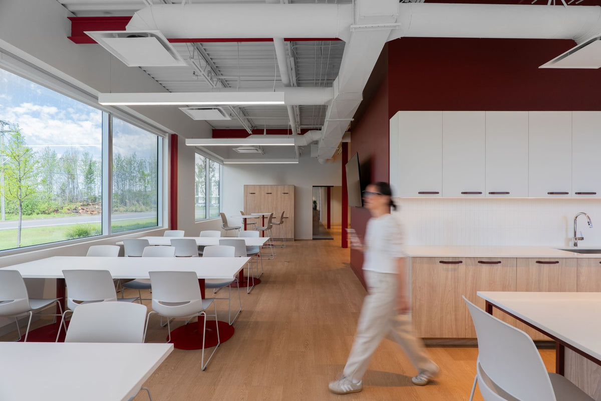 Cafétéria corporative avec tables blanches, cuisine intégrée bois, mur bordeaux et grandes fenêtres — Beauce Atlas