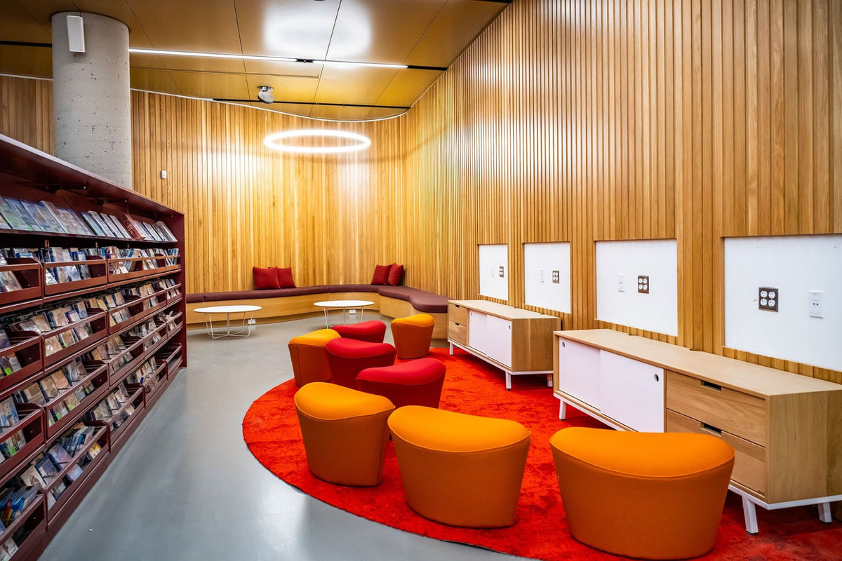 Espace lounge bibliothèque avec mobilier contemporain - Fauteuils orange, banquette sur mesure et revêtement bois