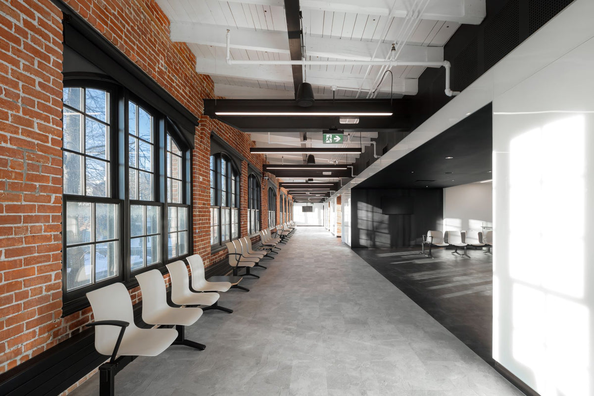 Espace d’attente lumineux avec chaises modernes et murs de brique dans l’édifice patrimonial F.-X.-Drolet à Québec