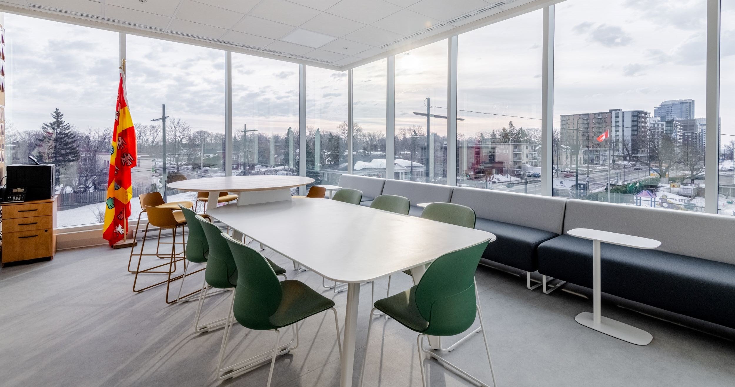 Salle de formation moderne avec table blanche et chaises vertes - mobilier de formation professionnel avec banquette noire et vue panoramique urbaine