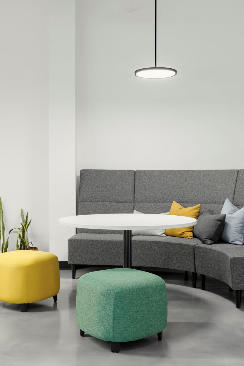 Coin lounge corporatif moderne avec canapé modulaire gris, poufs colorés jaune et vert menthe, et table d'appoint minimaliste. Espace détente professionnel au design contemporain avec luminaire suspendu LED et mobilier confortable pour favoriser la collaboration et le bien-être au bureau.