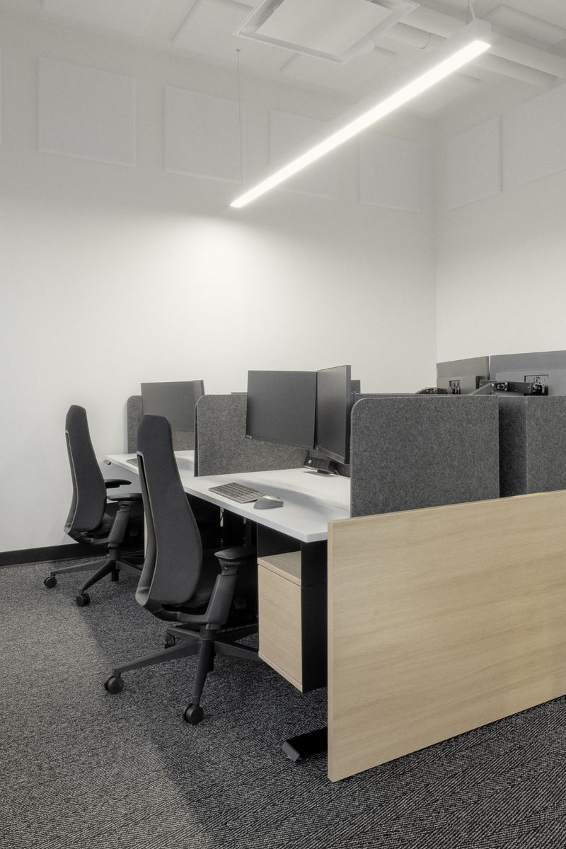 "Postes de travail en îlot avec bureaux benching en bois clair, panneaux acoustiques gris et chaises ergonomiques noires pour maximiser l'espace et la collaboration. Configuration de bureau moderne à aire ouverte avec rangement intégré, éclairage LED linéaire et design minimaliste pour environnement professionnel productif."