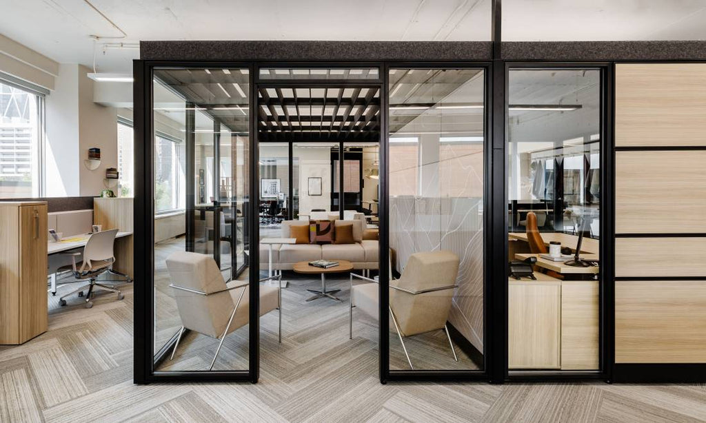 Bureaux modernes avec cloisons vitrées, espace lounge avec fauteuils beiges, table basse et zones de travail lumineuses.